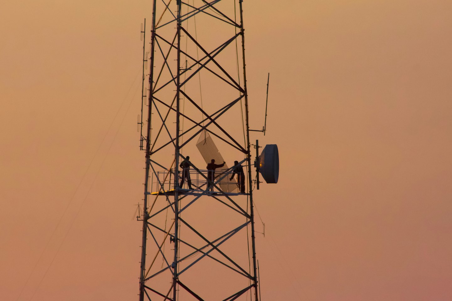 Technicians work on a lattice tower against a blue sky.
